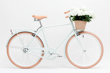 A modern bicycle stands upright against a white background, featuring a wicker basket filled with vibrant flowers, showcasing a chic and fresh look