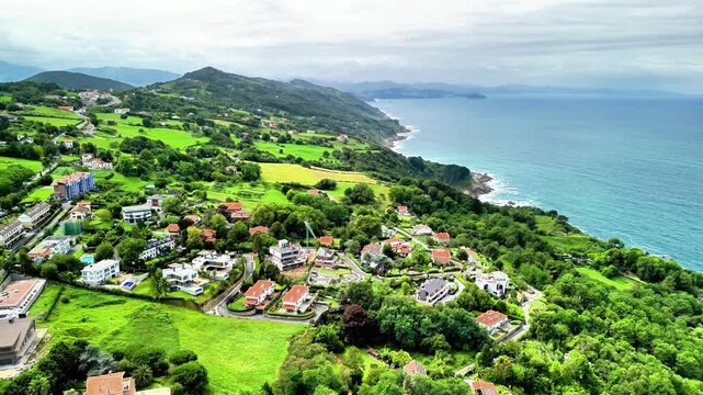 An aerial view clearly showcases a vivid and lush green coastal landscape featuring charming homes scattered throughout