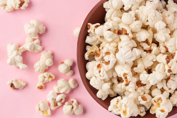 Tasty salty popcorn in a bowl on a pink background
