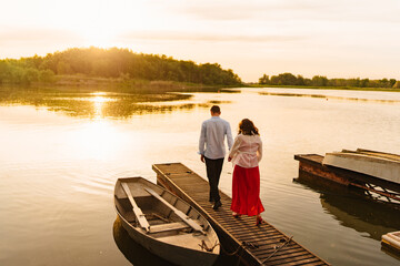 A man leads a pregnant woman along the pier on the river. 