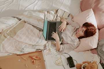 Relaxing on bed under cozy blankets while using laptop. Surroundings include snacks, phone with...