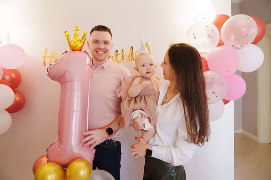 Happy and gentle parents hold baby daughter with birthday balloon decor. - Powered by Adobe