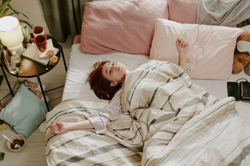 Person lying in bed while surrounded by soft blankets and pillows next to personal items on...