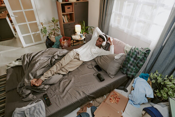 Relaxing in a cozy bedroom with modern decor and natural accents. Person lying on bed with casual clothing among scattered belongings, enjoying quiet moment