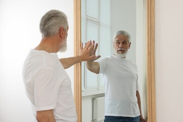 Obraz premium Handsome senior man looking at himself in mirror indoors