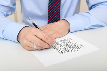 A nicely dressed man in a shirt and tie is solving a multiple choice test at a university, a...