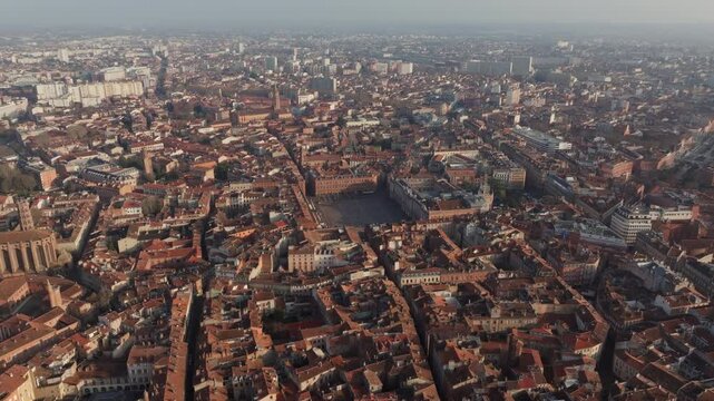 Aerial view capturing Toulouse historic center, highlighting Place du Capitole terracotta rooftops glowing under morning sunlight, revealing urban architectural splendor