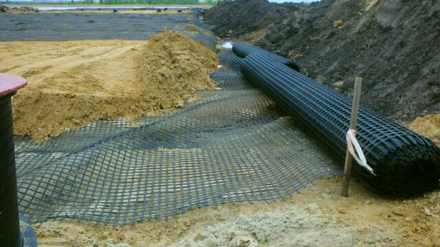 Geogrid and drainage pipes are installed on a road construction site, enhancing soil stability and managing water flow for a durable foundation