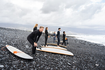 Surfing students warming up on volcanic beach before entering water