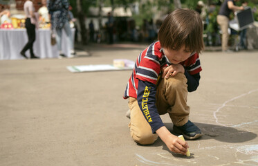 Fototapeta premium Cute little boy drawing chalk on the pavement outdoors.