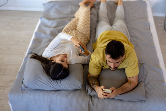 Man and woman using their smartphones while lying in bed, concept of lack of communication and technology addiction