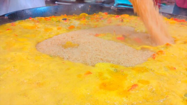 Arroz cae sobre paella hirviendo.