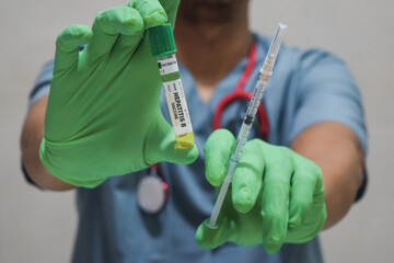 Text Hepatitis B vaccine of is written on a bottle with background of a doctor with a syringe in a medical glove mask. Medical concept