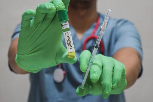 Text Hepatitis B vaccine of is written on a bottle with background of a doctor with a syringe in a medical glove mask. Medical concept