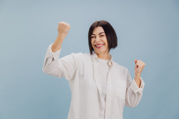 Enthusiastic mature woman celebrating success with raised fists on blue background