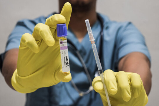 Text mRNA vaccine of is written on a bottle with background of a doctor with a syringe in a medical glove mask. Medical concept - Powered by Adobe