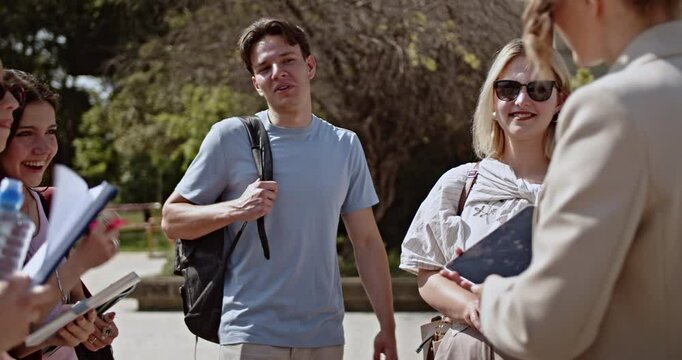 Energetic young people, likely college students, are happily engaged in conversation and laughter on a sunny campus.