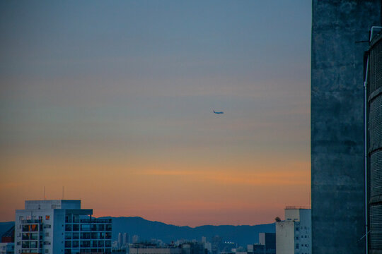 sunset in the urban center of São Paulo in a clear sky with a plane in close-up silhouette and mountain in the background