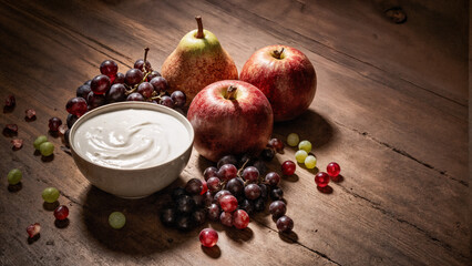 Bowl of creamy yoghurt with red apples, pears and grapes on a rustic wooden table