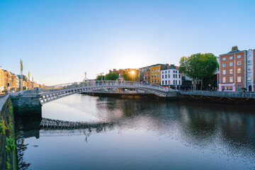 A view of Dublin’s Ha’penny Bridge over the River Liffey, framed by historic city buildings and a bright sky.