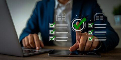 A businessperson in a navy blue suit interacts with glowing holographic checkmarks and documents above a wooden desk, with a silver laptop and blurred office background