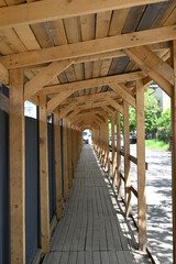 Long wooden walkway under construction canopy in urban area with greenery in the background