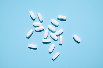 White oval tablets, vitamins, pills on blue background top view. Medical concept, minimalistic...