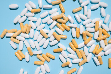 White oval tablets, vitamins and beige pills on blue background top view. Medical concept,...