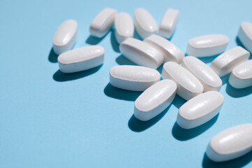 White oval tablets, vitamins, pills on blue background top view. Medical concept, minimalistic background with additives, dietary supplements. Health, self-care, pharmaceuticals