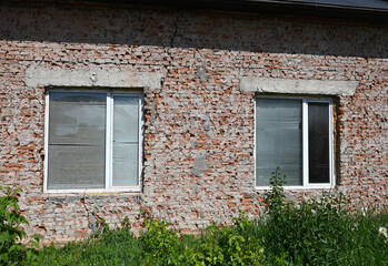 Rustic brick house exterior with two windows surrounded by greenery on a sunny day