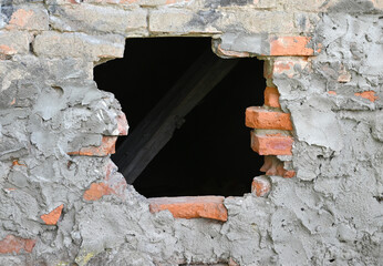 Hole in the wall revealing wooden beams in an old brick structure located outdoors in a rural...