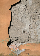 Cracked wall revealing brick beneath worn plaster in urban setting under natural sunlight