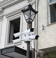 Security cameras mounted on a lamp post in an urban setting observe street activity during the day