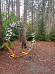 Fototapeta premium Romantic forest wedding altar featuring a hexagon arch adorned with roses and eucalyptus, surrounded by tall pine trees.