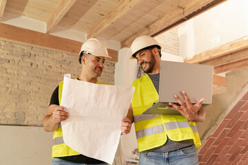 Male Architect discussing with engineer blueprint and using laptop during house renovation