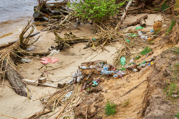 Pollution on a riverbank with plastic waste and driftwood.