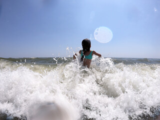Powerful ocean waves splashing on child girl in summer vacation
