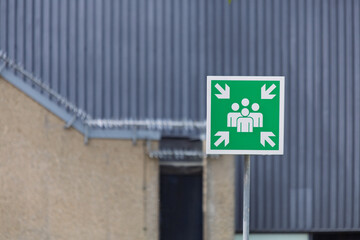 A vivid green emergency assembly point sign, clearly indicating a designated safe gathering area.