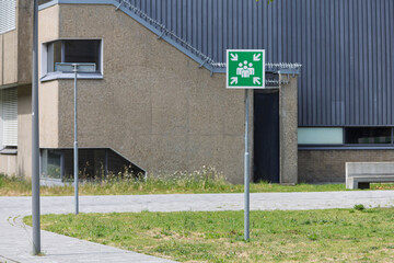 A bright green emergency assembly point sign stands prominently in front of a modern building, emphasizing safety.