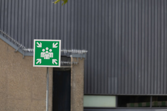 A prominent green emergency assembly point sign, set against a modern building facade, highlighting safety and preparedness.