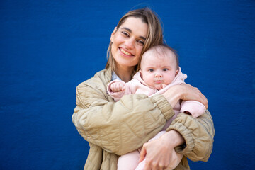 Happy mother smiling while holding baby close in front of a bright blue wall