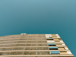 Low angle view of a contemporary apartment building with balconies and blue awnings against a clear...