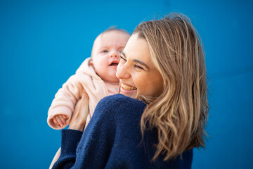 young mother holds her baby close, both smiling against a blue background