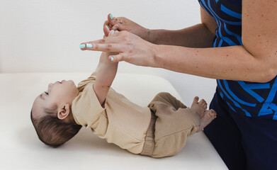 Physical therapist working with infant during neurological pediatric exam for test on newborn reflexes. Pull to sit or arm traction test