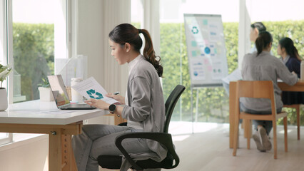 The way forward save the planet earth Gen Z female asia people go green net zero waste control ESG audit office desk. Young adult woman asian SDG carbon credit tax auditor busy happy work using laptop