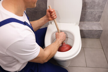 Plumber unclogging toilet with hand plunger indoors, closeup