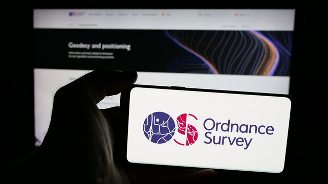Stuttgart, Germany - 06-09-2025: Person holding mobile phone with logo of British mapping agency Ordnance Survey (OS) on screen in front of web page. Focus on phone display.
