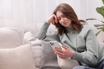 Cyber bullying. Upset teenage girl with smartphone on sofa at home