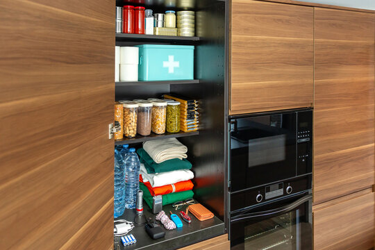 Modern kitchen pantry organized with food and drink supplies, canned goods, non perishable items and clothes. Cupboard stocked for potential emergencies or food scarcity. 72 hours survival kit concept