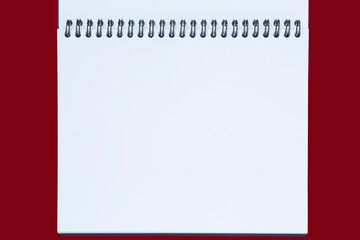 blank white page of opened sketchbook with spiral binder against red background